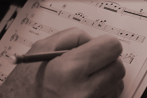Close up picture of a hand and pencil making notes on sheet music